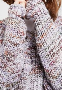 Pull en tricot dans un fil doux et multicolore, featuring des nuances de lavande, de crème et des touches d'orange. Poignets côtelés avec une coupe ample.