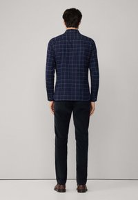 Camicia a righe blu navy con maniche lunghe, caratterizzata da un colletto strutturato e polsini con bottoni. Abbinate a pantaloni scuri e scarpe marroni.