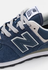 Sneaker blu navy realizzato in materiali scamosciati e in rete, con lacci grigi, un grande logo grigio "N" e una linguetta imbottita bianca. Suola strutturata.
