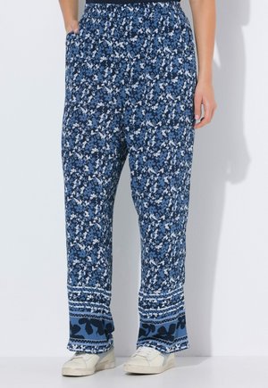 Blå løstsiddende bukser med blomsterprint, elastisk talje, sidelommer og brede sømme, båret med hvide sneakers.