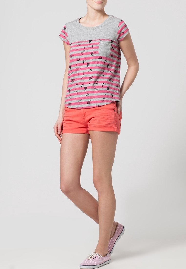 Grijs-roze gestreept T-shirt met een zakje en speelse patronen, gecombineerd met koraalkleurige shorts en slippers met polkadots. Casual zomerse outfit.