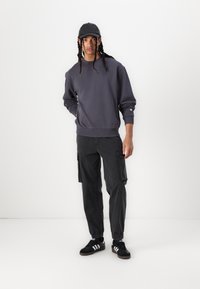 Mörkgrå sweatshirt med avslappnad passform, med ribbade muddars. I kombination med svarta cargobyxor, prydda med sidofickor. Svarta sneakers med vita ränder.