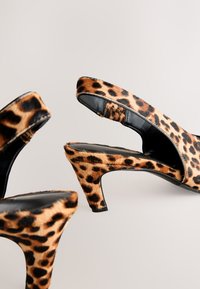 Paire d'escarpins slingback à talons hauts imprimé léopard avec semelles intérieures noires sur un fond neutre clair.