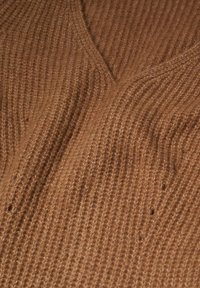 Tissu marron tricoté présentant un col en V avec une texture côtelée en relief et de subtiles variations de teinte. Aspect doux et confortable.