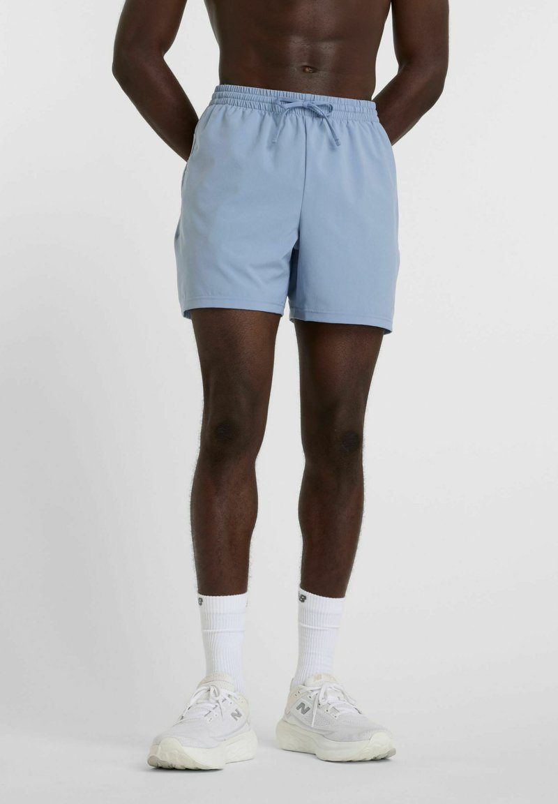 Light blue swim shorts with an elastic waistband and drawstring, featuring a smooth texture and above-knee length. Worn with white sneakers.