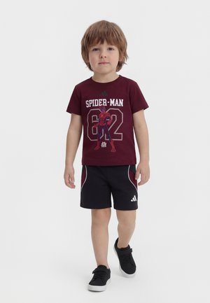 Garçon marchant portant un T-shirt Spider-Man bordeaux, un short Adidas noir avec des accents bordeaux, et des baskets noires avec des semelles blanches.