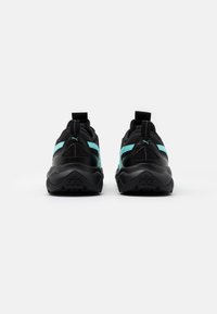 Chaussures de sport noires avec des accents turquoise, dotées d'une semelle texturée, d'un col rembourré et de languettes pour faciliter l'enfilage.