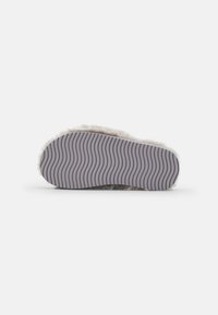 Light gray slipper sole with a plush texture and ridged pattern for grip. Material appears soft and fuzzy surrounding the base.