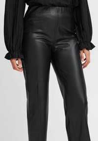 Pantaloni neri in ecopelle con vita alta, vestibilità slim e texture lucida. Presentano cuciture laterali e una finitura liscia, ideali per vari outfit.