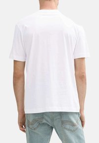 T-shirt en coton blanc à manches courtes, col rond et texture lisse. Coupe légèrement ample. Porté avec un jean délavé.