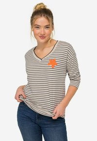 Randig v-ringad tröja i beige och marinblå med en orange stjärnformad patch på bröstet. Långa ärmar och avslappnad passform, tillverkad av mjukt tyg.