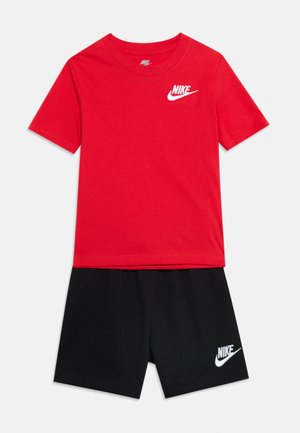 T-shirt rouge Nike à manches courtes avec logo blanc sur la poitrine, associé à un short noir Nike avec logo blanc sur la jambe gauche.
