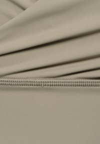 Beżowa elastyczna tkanina z marszczeniami, o gładkiej fakturze i starannie wykończonym brzegu u dołu.