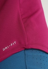 Maglione Dri-FIT magenta con texture liscia e finitura delle cuciture, abbinato a tessuto blu con piccoli fori di ventilazione.