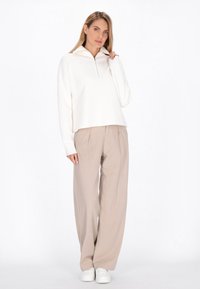 Hvid zip-up sweater med høj krave, parret med beige vide bukser og hvide sneakers. Glat stof med afslappet pasform.