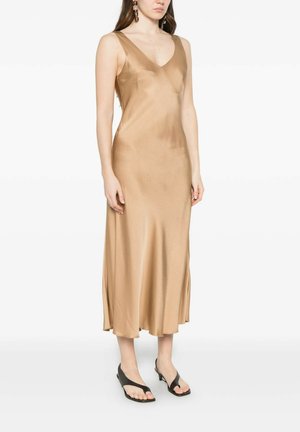 Donna che indossa un abito midi in raso color champagne senza maniche abbinato a tacchi aperti neri con cinturino a infradito e orecchini pendenti geometrici.