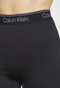 Leggings nere a costine con una vestibilità aderente e vita elasticizzata, caratterizzati dal logo "Calvin Klein" in grigio chiaro.