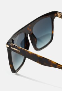 Occhiali da sole tartarugati con finitura lucida, lenti grigie a gradiente e dettagli dorati sulla montatura e sulle tempie. Presentano un audace design squadrato.