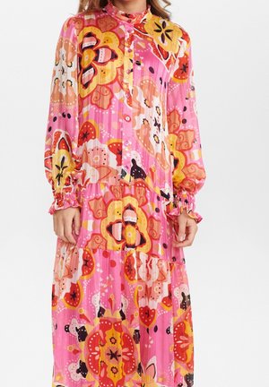 Różowa sukienka z długim rękawem, zapinana na guziki z przodu, z warstwową spódnicą ozdobioną dużymi pomarańczowymi, żółtymi i czerwonymi kwiatowymi wzorami.
