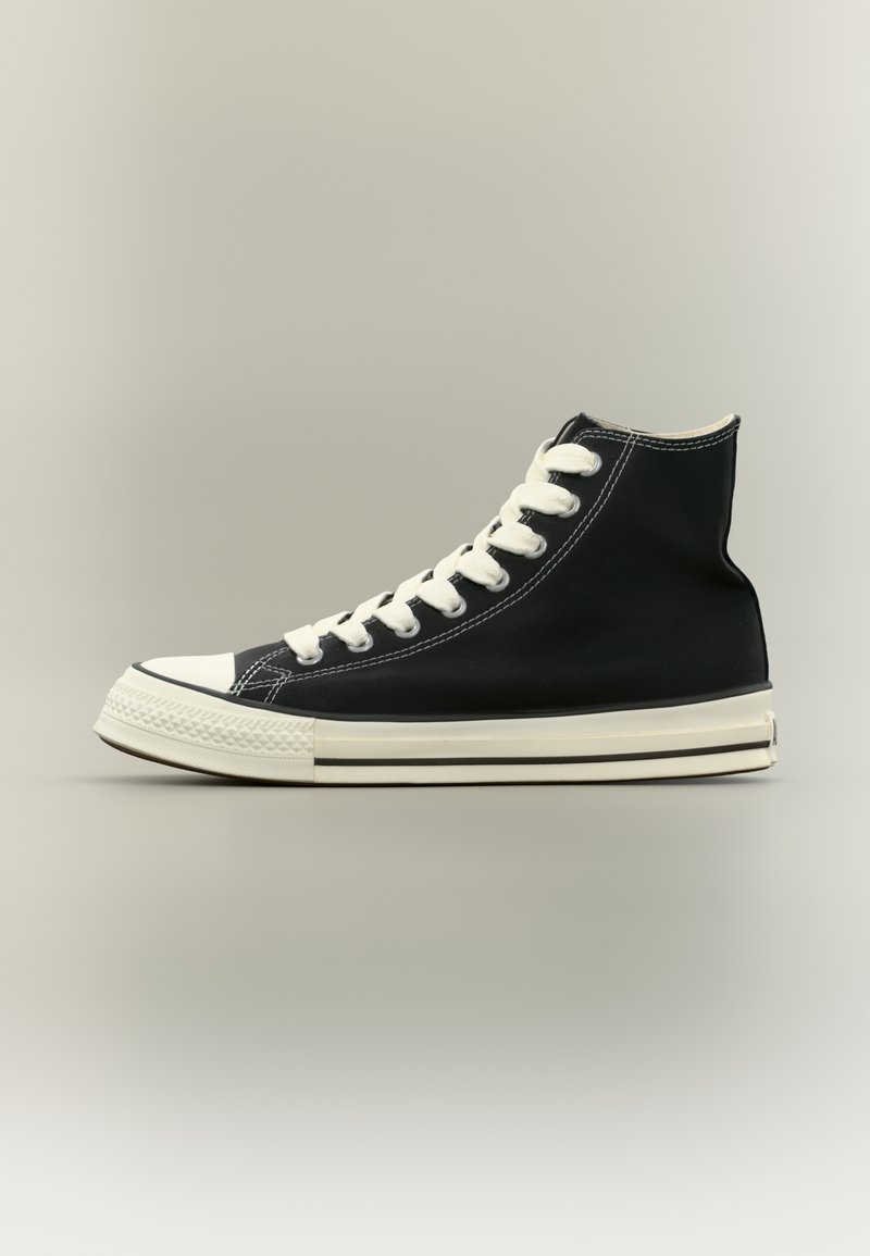 Μαύρο high-top πάνινο αθλητικό παπούτσι με λευκή καουτσούκ σόλα, λευκά κορδόνια και λευκή μύτη σε ουδέτερο γκρι φόντο.