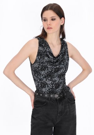 Femeie purtând un top fără mâneci, negru și gri cu imprimeu floral și decolteu drapat, blugi negri cu talie înaltă, cercei cerc și o curea neagră cu ochiuri argintii.