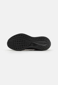 Semelle extérieure de sneaker noire avec un motif de grip texturé, présentant une légère courbe au niveau du talon et une pointe lisse et arrondie. Logo de la marque visible.