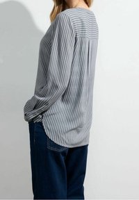 Grijs en witte gestreepte blouse met lange mouwen, ronde halslijn en plooidetail aan de achterkant, gecombineerd met donkerblauwe jeans.