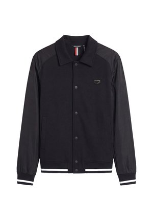 Zwarte varsityjas met drukknopen, lange mouwen, witte strepen op manchetten en zoom, en een klein geborduurd logo op de borst.