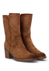 Botas de tobillo de ante marrón con tacón cuadrado, que presentan una textura suave, detalles de costura y un panel lateral elástico para un uso fácil.