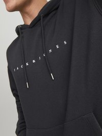 Black hoodie with a drawstring, featuring a white "JACK & JONES" logo across the chest. Made of soft fabric with a classic fit.
