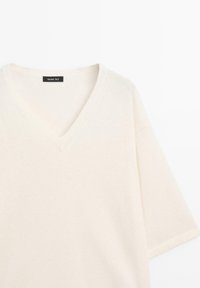 V-neck, short-sleeve top in soft cream fabric. Features a relaxed fit and subtle texture. Label: Massimo Dutti.