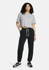 Grijze cropped t-shirt gecombineerd met zwarte joggers met een elastische tailleband en witte trekkoord, aangevuld met zwarte sneakers.