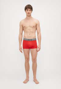 Red boxer shorts with a black and white checkered elastic waistband featuring the brand name “Moschino” on the front.