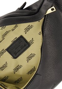Schwarze Lederhandtasche mit strukturiertem Oberflächen, goldfarbener Reißverschluss und beigem Futter mit wiederholtem Branding. Innenschild auf dem Stoff genäht.