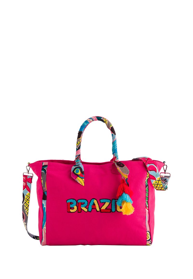 Bolsa de lona rosa con "BRAZIL" bordado en negro. Presenta una correa y acentos estampados, y una colorida decoración de pompones en el lado.