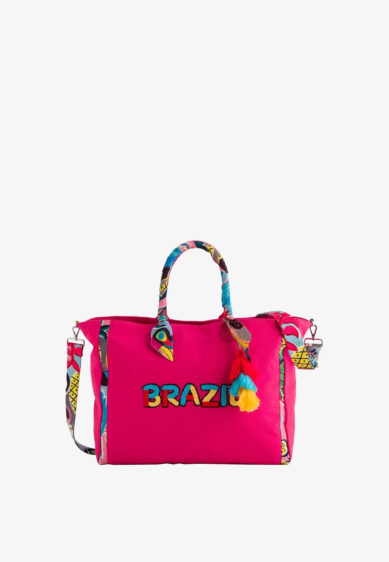 Bolsa de lona rosa con "BRAZIL" bordado en negro. Presenta una correa y acentos estampados, y una colorida decoración de pompones en el lado.