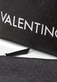 Black textured leather bag featuring a subtle logo pattern, with prominent white "VALENTINO" lettering and a zippered accessory pouch.