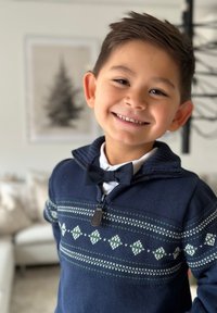 Laivaston sininen neule, jossa on vihreä ja valkoinen geometrinen kuvio, vetoketjukaulus, yhdistettynä valkoisen paidan ja mustan solmion kanssa. Tasainen neulepinta, rento istuvuus.