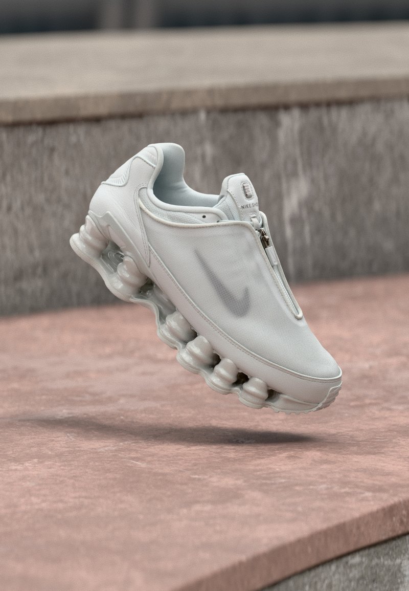 Λευκά παπούτσια Nike με λεία, υφασμάτινη επιφάνεια κορυφαίου τμήματος και κλείσιμο με φερμουάρ, με καμπυλωτή σόλα που διαθέτει ορατές μαξιλαράκια απορρόφησης κραδασμών.