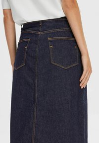 Jeans krilo, temno modro, srednje dolžine s ravnim krojem. Ima dva zadnja žepa in vidne oranžne šive. Gladka tekstura.