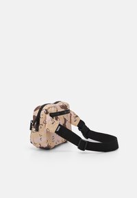 Malá crossbody taška v béžovém a hnědém abstraktním vzoru, vyrobená z odolné tkaniny, s černými zipy a nastavitelným popruhem.