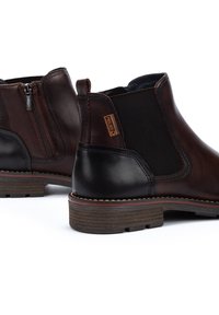 Bottines en cuir marron avec des panneaux élastiques sur les côtés, une fermeture éclair et un talon noir contrastant. Surface texturée avec une semelle marron.
