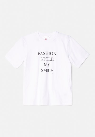 Balta kokvilnas T-kreklu ar īsām piedurknēm un apaļu kakla izgriezumu, ar uzrakstu "MODA MAN NOZAGA SMIEKLU" drukātos treknajos melnajos burtos.