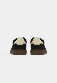 Sneakers negre cu accente crem, material din suede, design low-top, vârf rotunjit și talpă exterioară din cauciuc texturat de culoare brună. Vedere din spate care arată detalii de cusătură.