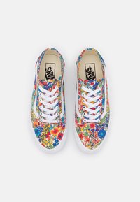 Paire de baskets Vans blanches avec un motif floral coloré et des lacets blancs, vues de dessus sur un fond uni.