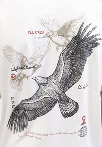 T-shirt blanc avec des illustrations graphiques d'oiseaux en noir et gris, avec du texte rouge. Les détails incluent des formes triangulaires et une icône de globe.
