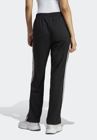 Svarta träningsbyxor med en avslappnad passform, med vita sidostrick. Tillverkade av lätt material med ett elastiskt midjeband för komfort.