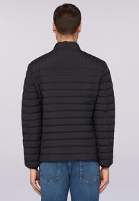 Černá prošívaná bunda s strukturovaným límcem a dlouhými rukávy. Nošena s modrými denimovými džíny. Texturovaná látka.