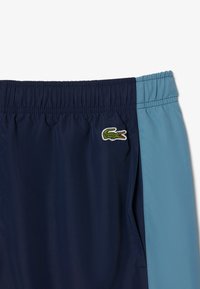 Navyblauwe en lichtblauwe kleurgebroken zwembroek met een elastische tailleband en het Lacoste krokodillenlogo aan de voorkant links.