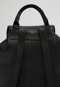 Sac à dos en cuir noir texturé montrant la poignée supérieure et deux bretelles réglables contre un fond uni.